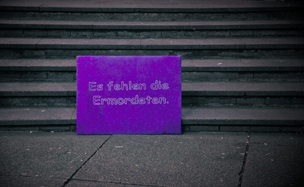 Auf einer menschenleeren Treppe steht einsam ein einzelnes Schild, auf dem steht: "Es fehlen die Ermordeten"